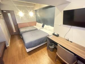 a small room with a bed and a desk with a tv at BiBi Hotel コンベンションベイ in Ginowan