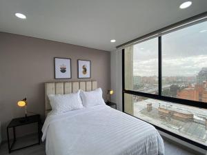 - une chambre avec un lit blanc et une grande fenêtre dans l'établissement Amplio apartamento con excelente vista, à Bogotá