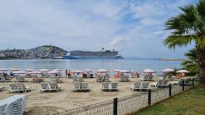 a beach with chairs and umbrellas and a cruise ship at Condo Reina, Kusadasi in Kusadası