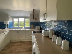 una cocina con armarios blancos y azulejos azules en la pared en Winstitchen Cottage, en Simonsbath