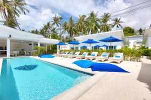a swimming pool with blue umbrellas and chairs at La Perle Resort Koh Samui in Mae Nam
