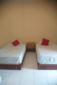twee bedden in een kamer met rode kussens erop bij Nushe Hostel in Nusa Penida