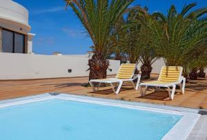 two chairs and a swimming pool with palm trees and a house at Riviera Park 2b, central 2 bed in Puerto del Carmen