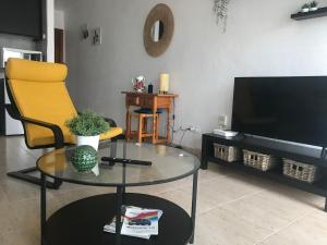 sala de estar con mesa de cristal, silla amarilla y TV en One bedroom bungalow Playa Bastian Costa Teguise, en Costa Teguise