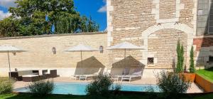 a pool with chairs and umbrellas next to a brick building at Le Clos des Riceys - La Villa Lombardi in Les Riceys