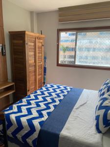 a bedroom with a blue and white bed and a window at Suíte Itaipu Mar in Vila Velha