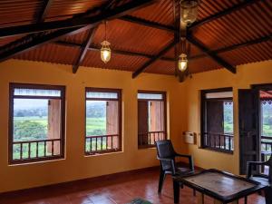 ein Zimmer mit Tisch, Stühlen und Fenstern in der Unterkunft Vanacara in Sawantwadi