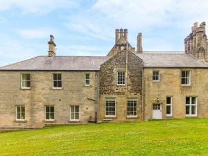 uma antiga casa de pedra com um campo de relva em frente em Coach House, Middleton Hall Estate em Belford