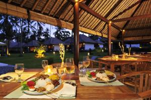 a wooden table with plates of food and wine glasses at Kubu Indah Dive & Spa Resort in Tulamben