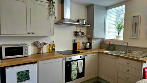 a kitchen with white cabinets and a microwave at The Ferns - Shared Garden Apartment With Parking in Darvel
