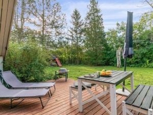 eine Holzterrasse mit einem Tisch, Stühlen und einem Sonnenschirm in der Unterkunft Holiday Home Ninni - 3-2km from the sea in Sealand by Interhome in Eskebjerg