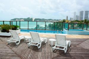 a group of white chairs sitting on a deck with a pool at Araça flat 308 - Lateral Vista Jardim in Natal