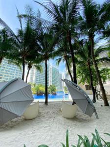 two chairs and umbrellas on a beach with palm trees at Condo in Azure Urban Resort Residences-Paranaque City in Manila