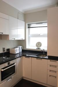 una cocina con armarios blancos y una ventana con reloj en Paddington Patio Apartment en Londres