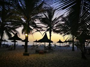 a beach with umbrellas and palm trees at sunset at Casa Lamar in Sanyang