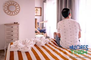 a man sitting on a bed looking out the window at a woman at Atlântida Dream T1 in Angra do Heroísmo