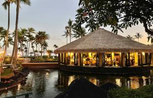 a restaurant with a thatch roof on a body of water at Kiahuna Paradise at Poipu beach, newly remodeled in Koloa