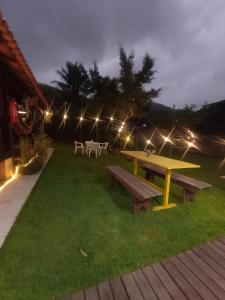 una mesa de picnic y bancos en el césped por la noche en Casa de praia cantinho do Saco 12 pessoas, en Angra dos Reis