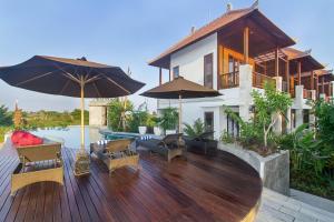 a wooden deck with chairs and umbrellas in front of a house at Odessa Village by Pramana Villas in Gianyar