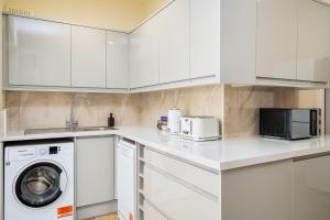 eine weiße Küche mit einer Waschmaschine und einer Mikrowelle in der Unterkunft Homely and Stylish Apartment with a garden in East Finchley in London