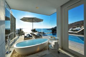 a bath tub in a bathroom with a view of the ocean at Mykonos Grand Hotel & Resort in Agios Ioannis Mykonos