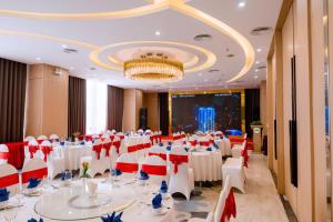 un salón de banquetes con mesas y sillas blancas y una lámpara de araña en Khách sạn Toàn Thắng Stone en Vinh