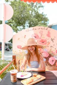 Una ragazza con un cappello di paglia seduta a un tavolo di Sidewalk Boutique Hotel a Ko Samed