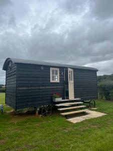 a black house with a door and stairs in a field at Shepherds Huts in Kidlington