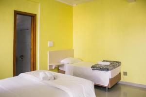 two beds in a room with yellow walls at Hotel Guaíba in Guaíba