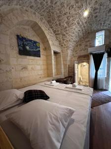 Cette chambre dispose d'un grand lit blanc et d'un mur en pierre. dans l'établissement Petra Hotel & Coffee House, à Şanlıurfa