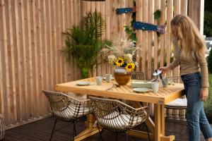 a woman standing at a wooden table with flowers on a fence at Morski Klimat Sasino domki z balią i kominkiem in Sasino