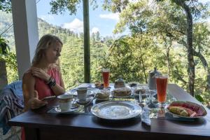 una mujer sentada en una mesa con comida y bebidas en Green Cloud Villa, en Ella