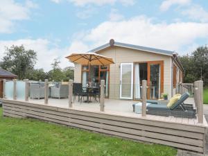 a house with a deck with a table and an umbrella at 32 Sanctuary Lodge in Pwllheli