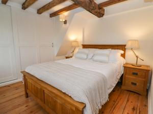 a bedroom with a bed with white sheets and wooden floors at 1 White House Cottages in Ross on Wye