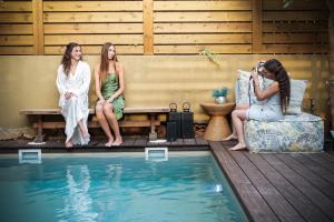 trzy kobiety siedzące na ławce obok basenu w obiekcie Laethos - the house of fun. w mieście Kfar Yona