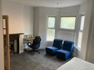 Cette chambre comprend deux chaises bleues, un bureau et une chaise. dans l'établissement En-suite room near, à Cardiff