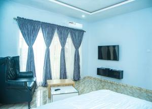een slaapkamer met een bed, een stoel en een televisie bij CIS Apartments in Abuja