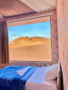 a bedroom with a view of the desert through a window at WADi RUM ALi CAMP in Wadi Rum