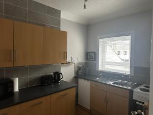 cocina con armarios de madera, fregadero y ventana en The Sandgate New Immaculate 1-Bed Apartment in Ayr, en Ayr