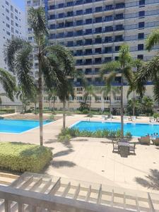 a pool with palm trees and a large building at Amigo's Place at Sea Residences in Manila