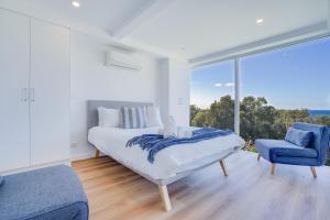 a white bedroom with a bed and a blue chair at Becker Bliss - Ocean views, 5 bedrooms, sleeps 12 in Forster
