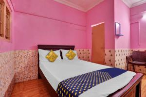 a bedroom with pink walls and a bed with yellow pillows at SPOT ON Sri Maheswari Lodge in Vijayawāda