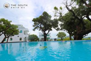 a swimming pool in front of a building with trees at The South-Dawn in Hengchun