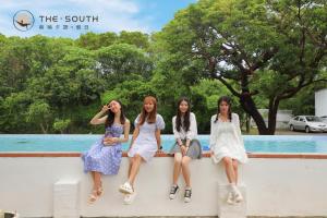 four girls sitting on a wall in front of a pool at The South-Dawn in Hengchun