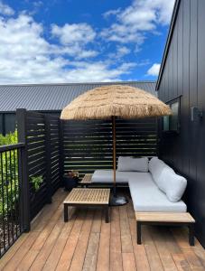 eine Terrasse mit einem Sofa, einem Sonnenschirm und einem Tisch in der Unterkunft Private by the beach in Whitianga