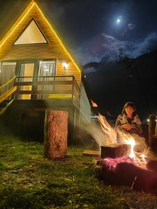 a woman sitting around a fire in front of a house at KAZBEGI COMPASS in Stepantsminda