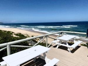 a deck with two white picnic tables and the beach at Sea-esta in Plettenberg Bay