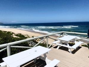 Una terraza con dos mesas de picnic blancas y la playa. en Sea-esta, en Plettenberg Bay