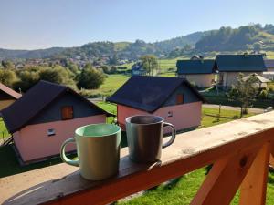 two coffee mugs sitting on a railing with a view of houses at Motylowe Wzgórze Zawóz Bieszczady in Zawóz