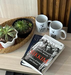 甘托克的住宿－LASA HOMES，一张桌子,上面有一本书,两个杯子和一本杂志